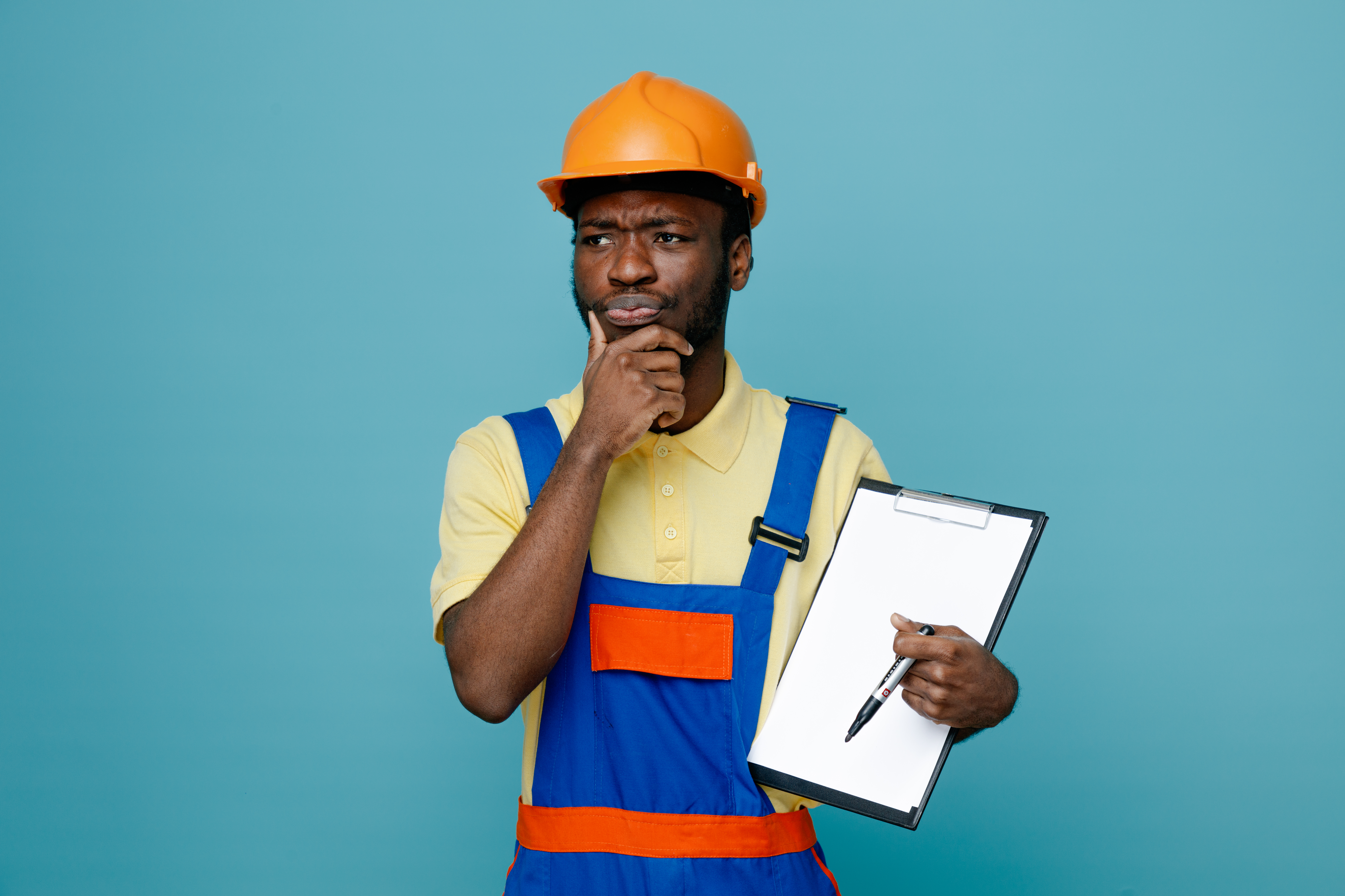 Home thinking grabbed chin young african american builder in uniform holding clipboard isolated on blue background